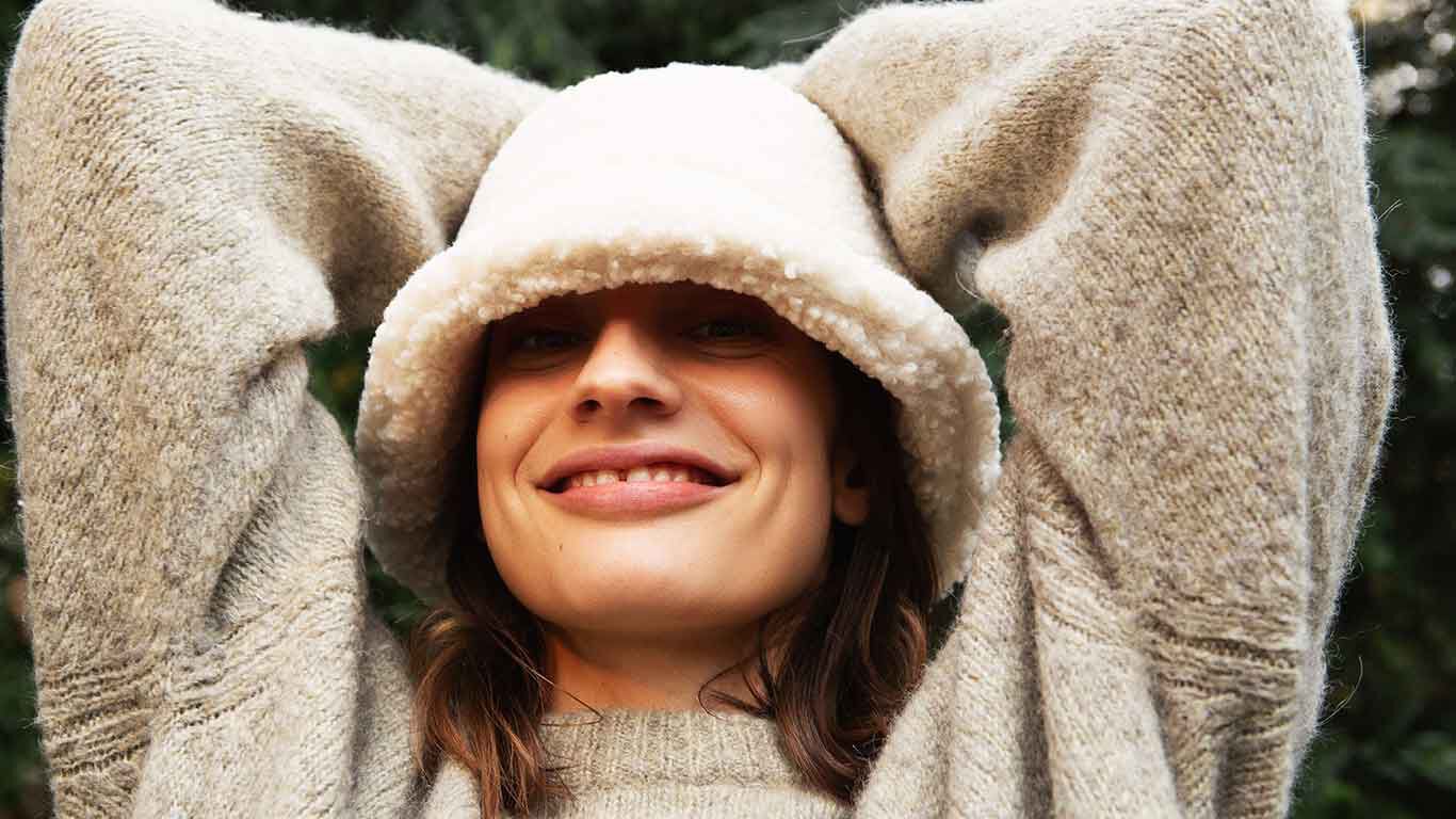 Vrouw met pluchen hoed kruist haar armen achter haar hoofd. 
